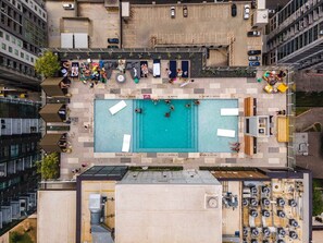 Ein Luftbild eines Dachpoolbereichs mit Schwimmbecken, Liegestühlen und einem Parkplatz.