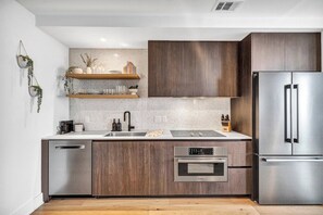 A modern kitchen with wooden cabinets, a stainless steel refrigerator, and a Bosch oven. - 2407 ATX Ranch on Rainey | Rooftop Pool, Lake Views, Rainey St Nightlife (Austin)