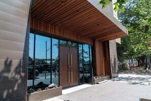 Ein modernes Gebäude mit einer großen Glasdoor, einer Holzlattendecke und einer gepflasterten Eingangszone.