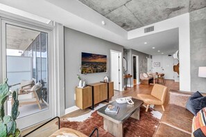 A spacious living area with a large window, a wooden cabinet, a leather sofa, and a coffee table. - 2407 ATX Ranch on Rainey | Rooftop Pool, Lake Views, Rainey St Nightlife (Austin)