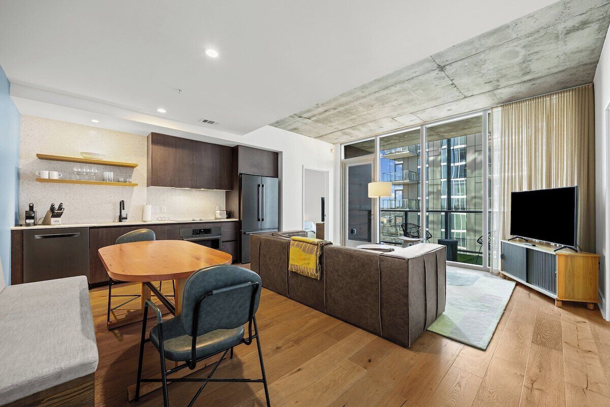 A modern kitchen with a dining area, a sofa, and a TV.
