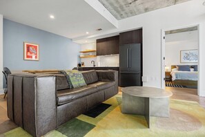 Ein modernes Wohnzimmer mit einer Ledersofa, einem runden Couchtisch und einer Küchenzeile mit dunklen Schränken und einem Kühlschrank.