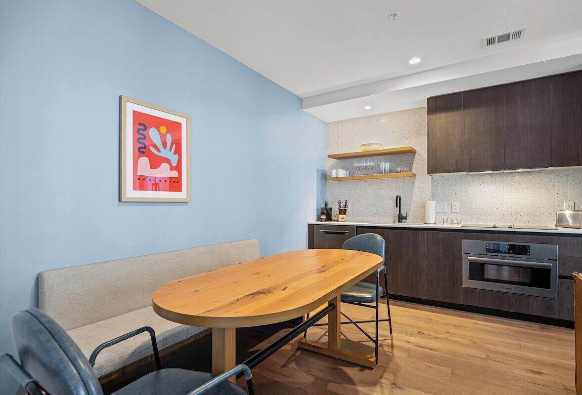 A modern kitchen with a wooden dining table, a sofa, and a kitchen island with a built-in oven.