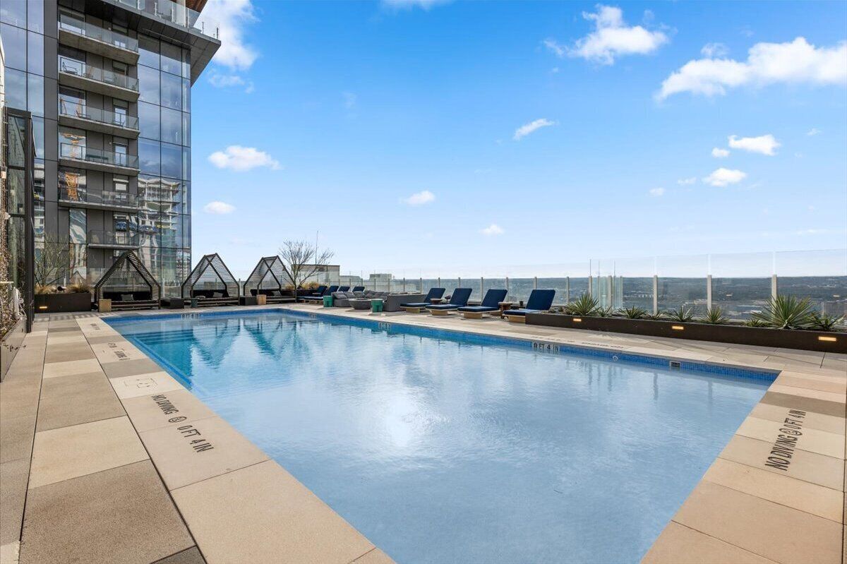 A rooftop pool with lounge chairs, a glass building, and a clear sky.