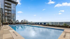 Ein Pool auf dem Dach mit Liegestühlen, ein Glasgebäude und ein klarer Himmel.