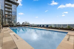 Ein Pool auf dem Dach mit Liegestühlen, ein Glasgebäude und ein klarer Himmel.