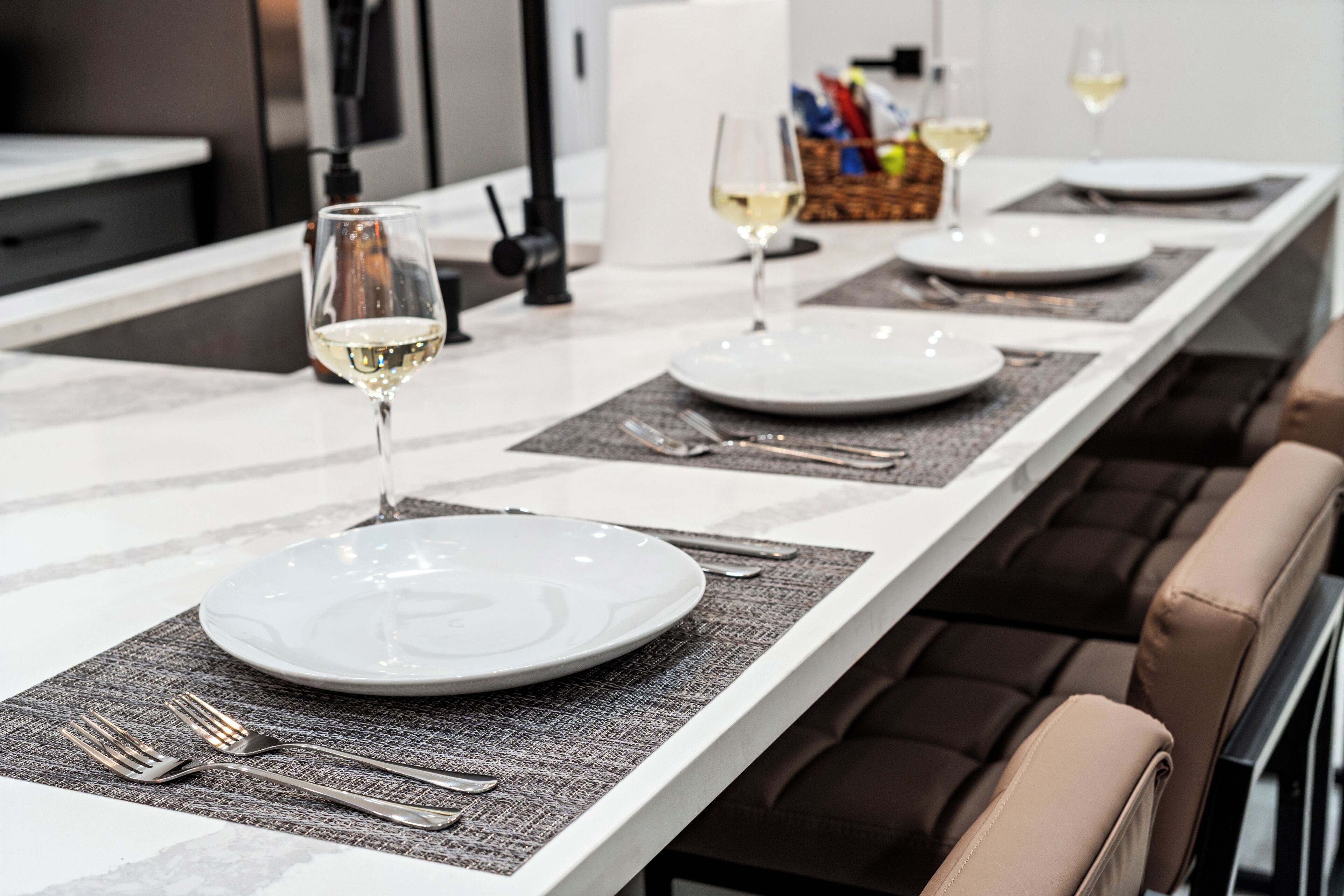 Une table à manger dressée avec des assiettes, des couverts et des verres, avec une cuisine moderne en arrière-plan.