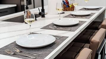 Une table à manger dressée avec des assiettes, des couverts et des verres, avec une cuisine moderne en arrière-plan.
