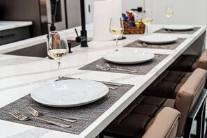 A dining table set with plates, cutlery, and glasses, with a modern kitchen in the background. - 4BR/4.5BA Luxury Dallas Retreat • Hot Tub + Fire Pit • Sleeps 15 (Dallas)