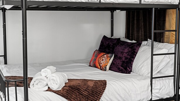 A bunk bed with white bedding, a brown throw blanket, and two patterned pillows. - 4BR/4.5BA Luxury Dallas Retreat • Hot Tub + Fire Pit • Sleeps 15 (Dallas)