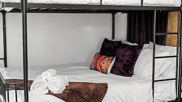 Un lit superposé avec une literie blanche, un plaid marron et deux coussins à motifs.