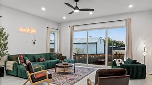 A spacious living room with a green sofa, two armchairs, a coffee table, and a large sliding glass door leading to an outdoor area. - 4BR/4.5BA Luxury Dallas Retreat • Hot Tub + Fire Pit • Sleeps 15 (Dallas)