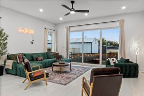 A spacious living room with a green sofa, two armchairs, a coffee table, and a large sliding glass door leading to an outdoor area. - 4BR/4.5BA Luxury Dallas Retreat • Hot Tub + Fire Pit • Sleeps 15 (Dallas)