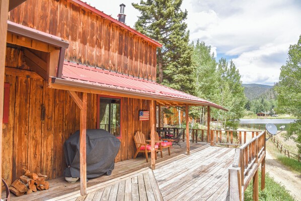 A wooden cabin with a covered porch, a grill, and a view of a lake and mountains.