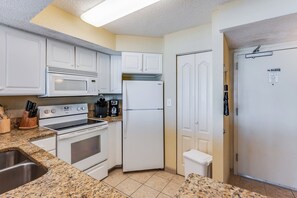 A kitchen with white cabinets, a microwave, a stove, a refrigerator, and a coffee maker. - Amazing Oceanfront Views at Carolinian with Pool (Myrtle Beach)
