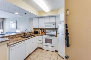 A compact kitchen with white cabinets, a microwave, a stove, and a refrigerator. - Amazing Oceanfront Views at Carolinian with Pool (Myrtle Beach)