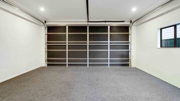 A clean, empty garage with a grey carpet, white walls, and a metal garage door.
