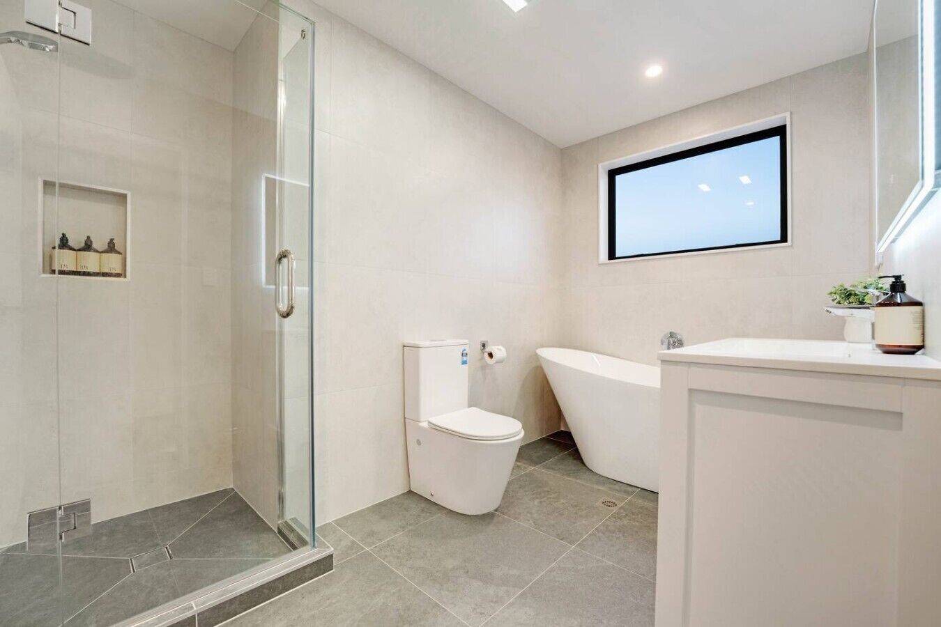 A modern bathroom with a glass shower enclosure, a toilet, a freestanding bathtub, and a vanity with a mirror.