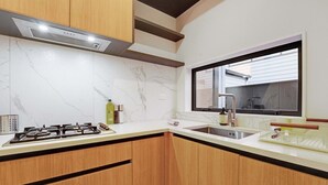 Una cocina con estufa a gas, un lavamanos, armarios de madera, un ventanal y salpicadero de mármol.