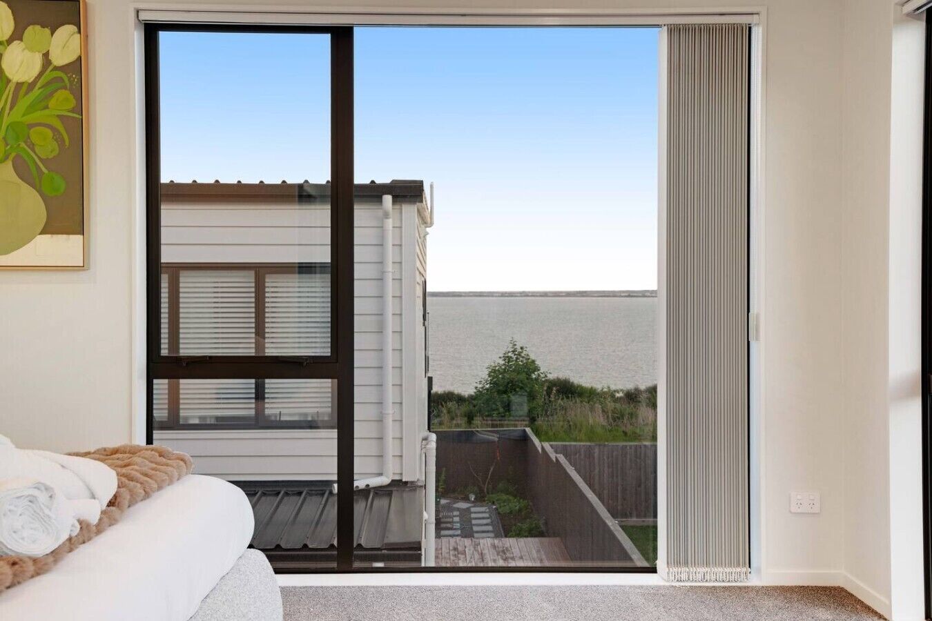 A bedroom with a large sliding glass door leading to a balcony with a view of the water.