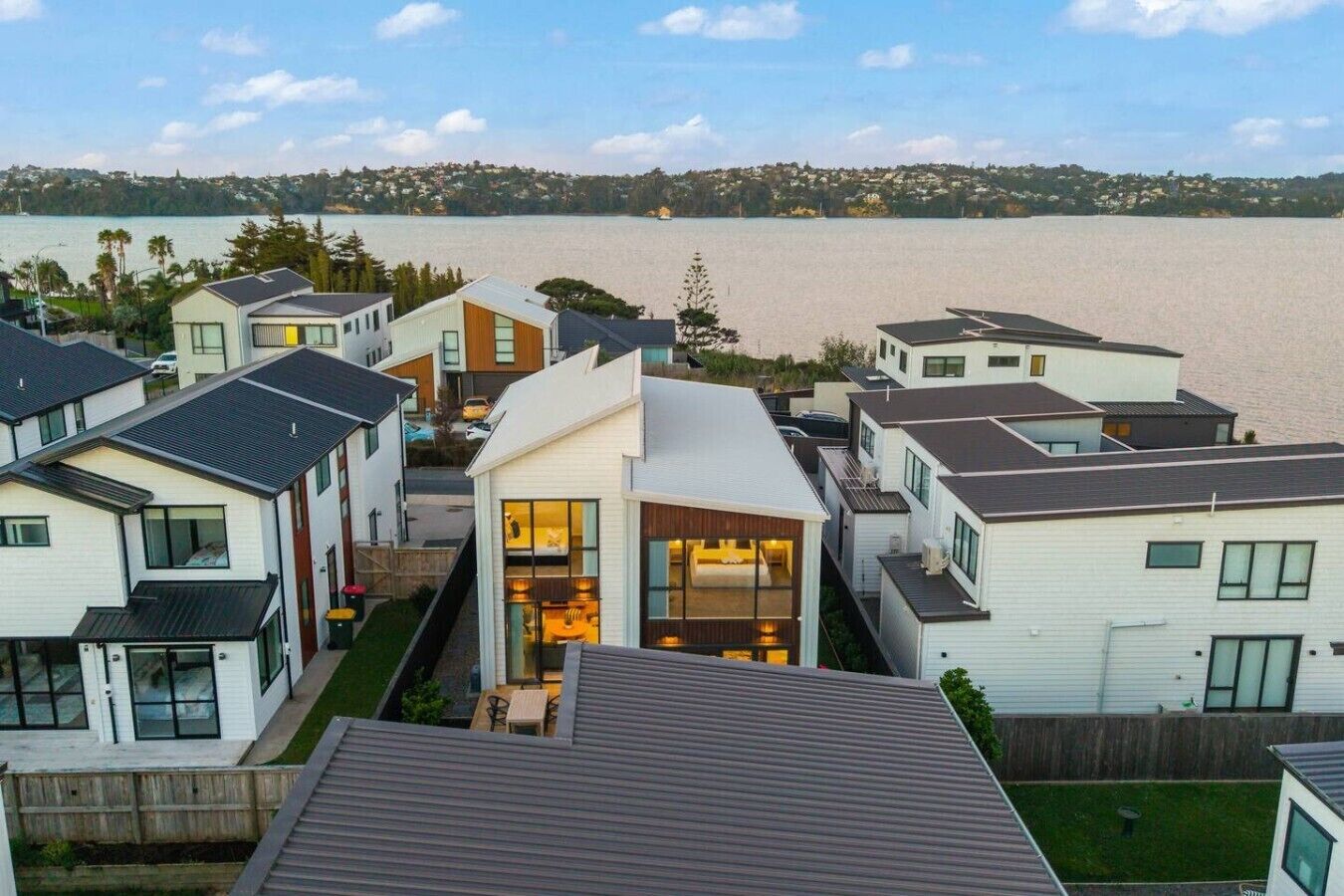A residential area with modern houses, a view of a lake, and a distant hill.
