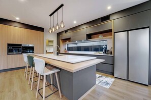 A modern kitchen with a central island, bar stools, built-in appliances, and a large refrigerator. - Hobsonville Family 5BR Sanctuary with Waterviews (Auckland West)