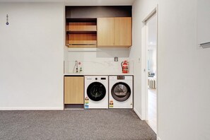 Un espace buanderie équipé de deux machines à laver, d’un extincteur et d’une petite étagère contenant des articles de toilette.