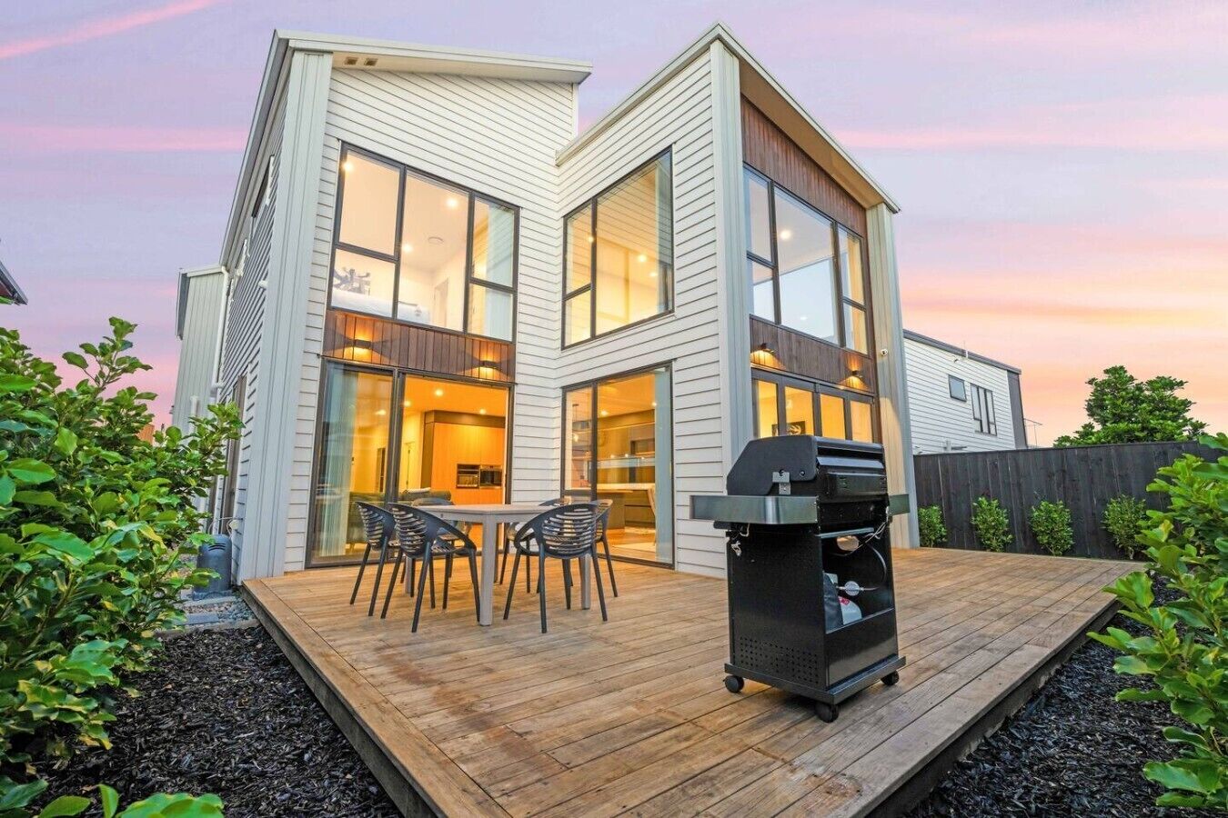 A modern house with a deck, a barbecue grill, and a dining area.