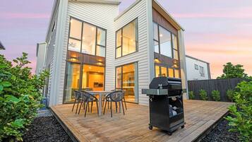 A modern house with a deck, a barbecue grill, and a dining area.