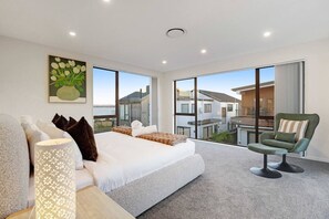 Une chambre moderne avec un grand lit, un fauteuil vert et une vue sur un quartier résidentiel.