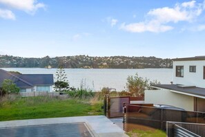 A residential property with a view of a lake, a swimming pool, and a hillside in the background. - Hobsonville Family 5BR Sanctuary with Waterviews (Auckland West)