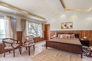 A hotel room with a large bed, two chairs, a small table, a nightstand, and a window with curtains. - Lakshmi Retreat (Kotagiri)