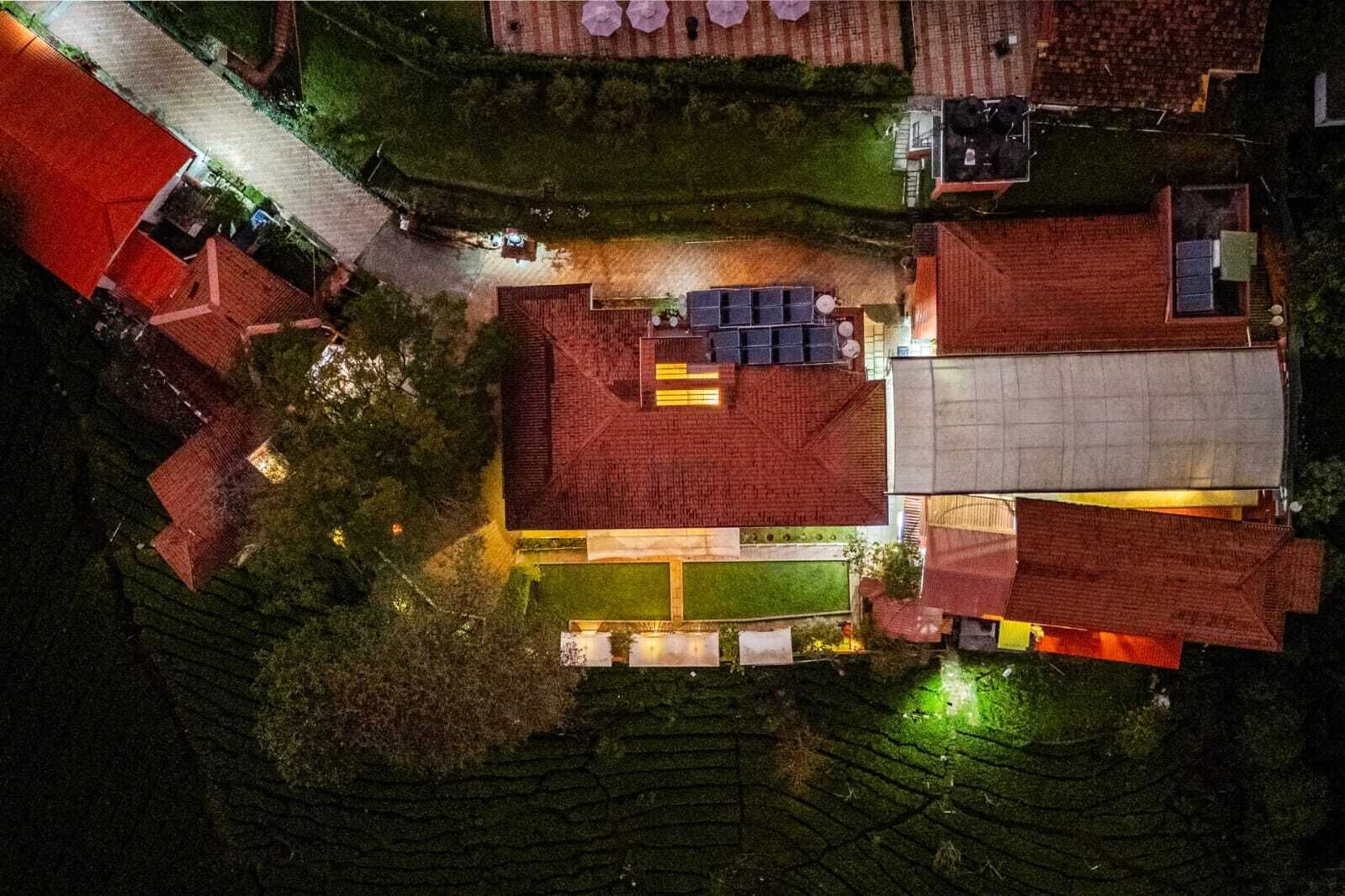 An aerial view of a residential area with multiple houses, a central open space with solar panels, and a well-maintained lawn.