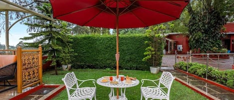 A round table with four white chairs and a red umbrella in a garden setting.