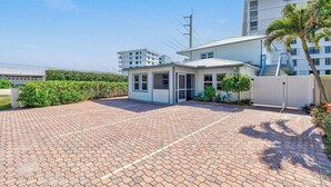 A modern building with a paved driveway, a small covered area, and a palm tree. - Best Location! Charming 1-Bedroom House Just Steps from Juno Beach (Juno Beach)