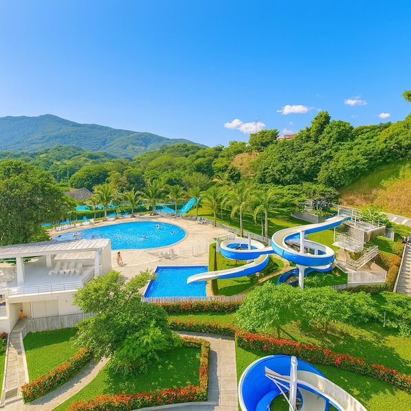 Un complexe hôtelier doté de plusieurs piscines, d’un toboggan aquatique et d’une végétation luxuriante.