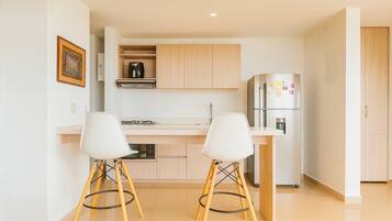 Una cocina moderna con dos taburetes blancos, un refrigerador de acero inoxidable y armarios de madera clara.