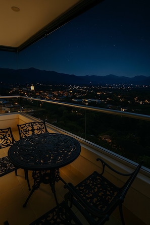 A balcony with a table and chairs, a view of a cityscape at night, and mountains in the distance. - Year Round Summer Pools and Water Slides Santa Fe (Santa Fe de Antioquia)