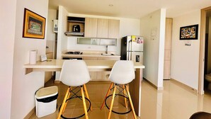 A compact kitchen with a gas stove, a refrigerator, and two white bar stools.
