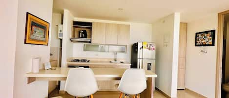 A compact kitchen with a gas stove, a refrigerator, and two white bar stools.