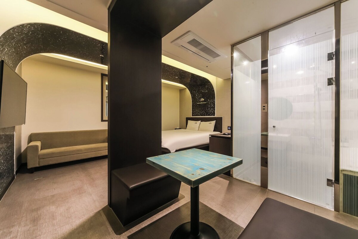 Una habitación de hotel moderna con una cama, un sofá, una mesita y baño privado.