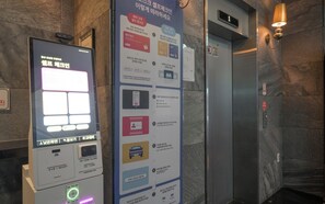 Een digitale informatiezuil met instructies voor het gebruik van een lift, een Samsung Pay kaartlezer en een QR-code scanner.