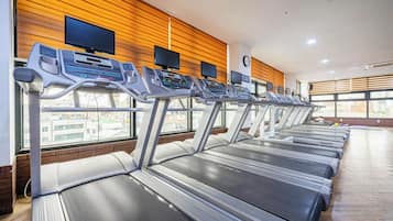 A gym with multiple treadmills, wooden wall panels, and large windows.