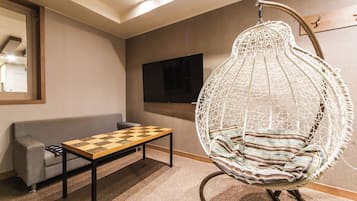 A room with a sofa, a table with a chessboard, a hanging chair, and a television mounted on the wall.