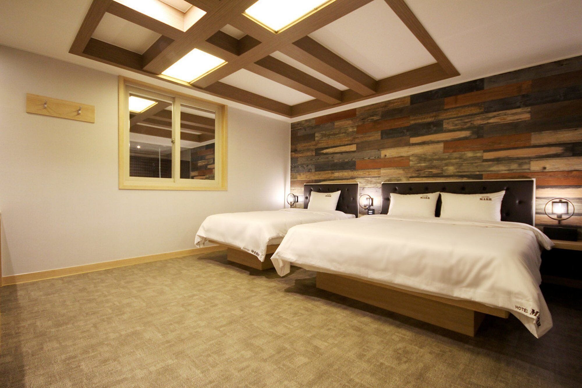 Habitación de hotel con dos camas, un ventanal grande y un panel de pared de madera.