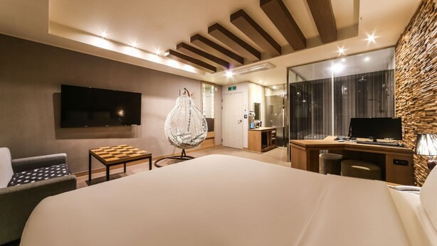 Une chambre d’hôtel avec un grand lit, un bureau avec un ordinateur, une télévision et un fauteuil suspendu.