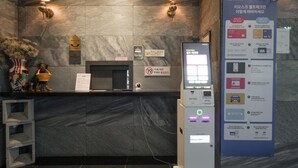 Un comptoir d’accueil d’hôtel avec un mur en marbre, un guichet d’accueil et un kiosque d’information numérique.