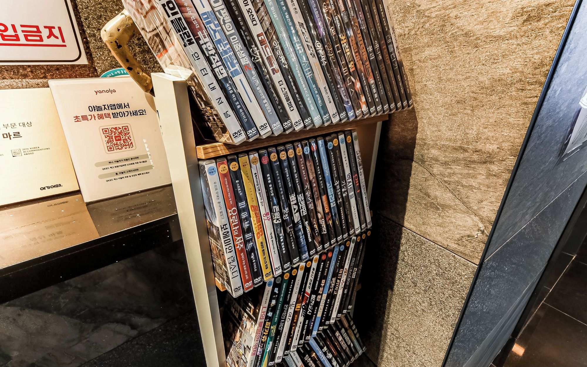 A DVD rack filled with various DVDs, a QR code, and a sign with Korean text.
