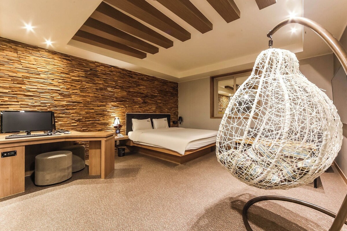 Una habitación de hotel moderna con una pared de madera, un escritorio con computadora, una cama y una lámpara colgante.