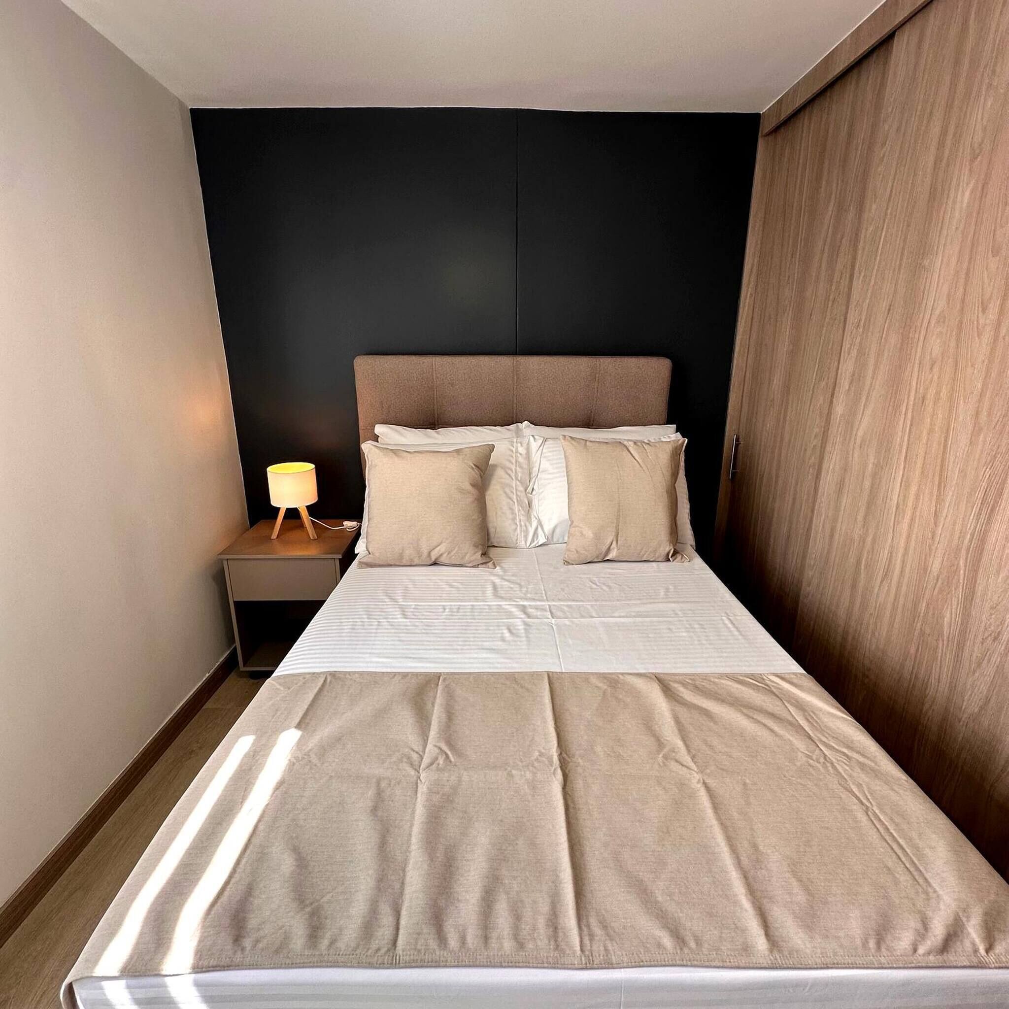 A neatly made bed with a headboard, a bedside lamp, and a wardrobe.